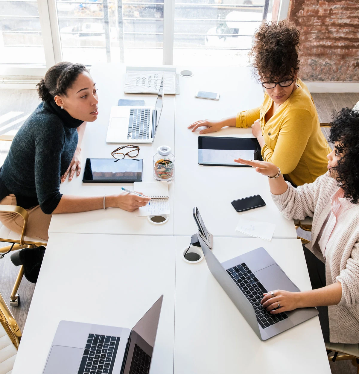 Three women exchanging ideas around a shared worktable